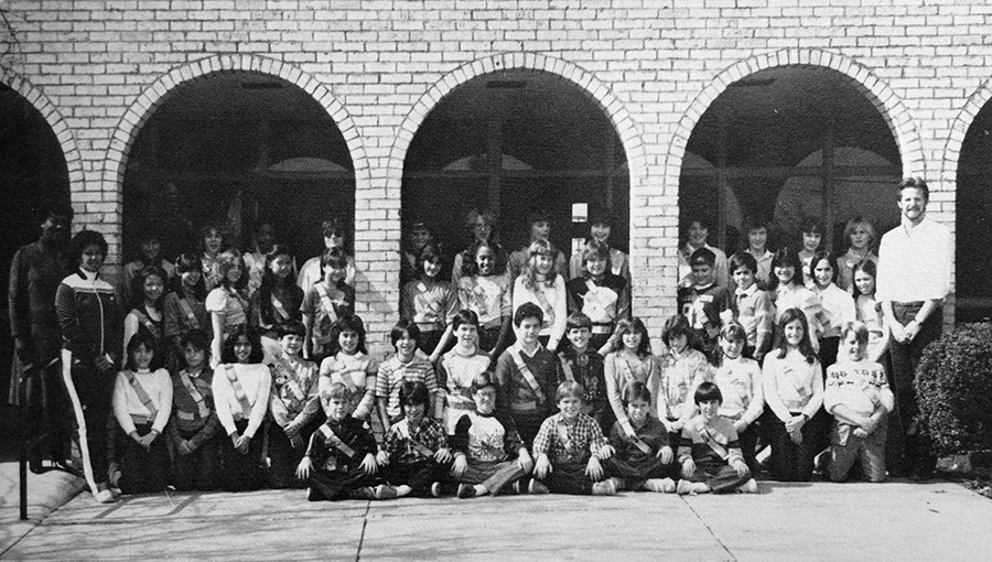 Black and white photograph from our 1983 to 1984 yearbook showing Forestdale’s Safety Patrol. A large group of approximately 45 students are posed under the archways that formerly lined the main entrance to our school. The students are wearing safety patrol belts and sashes. Several adults are pictured with the group. 